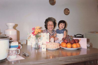 Young Chinese girl sitting at a kitchen table with her grandmother