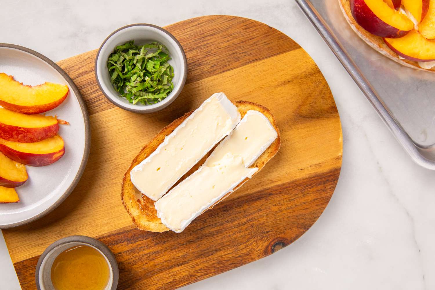 A serving tray with toasted bread topped with brie accompanied by sliced nectarines fresh herbs and a small cup of honey