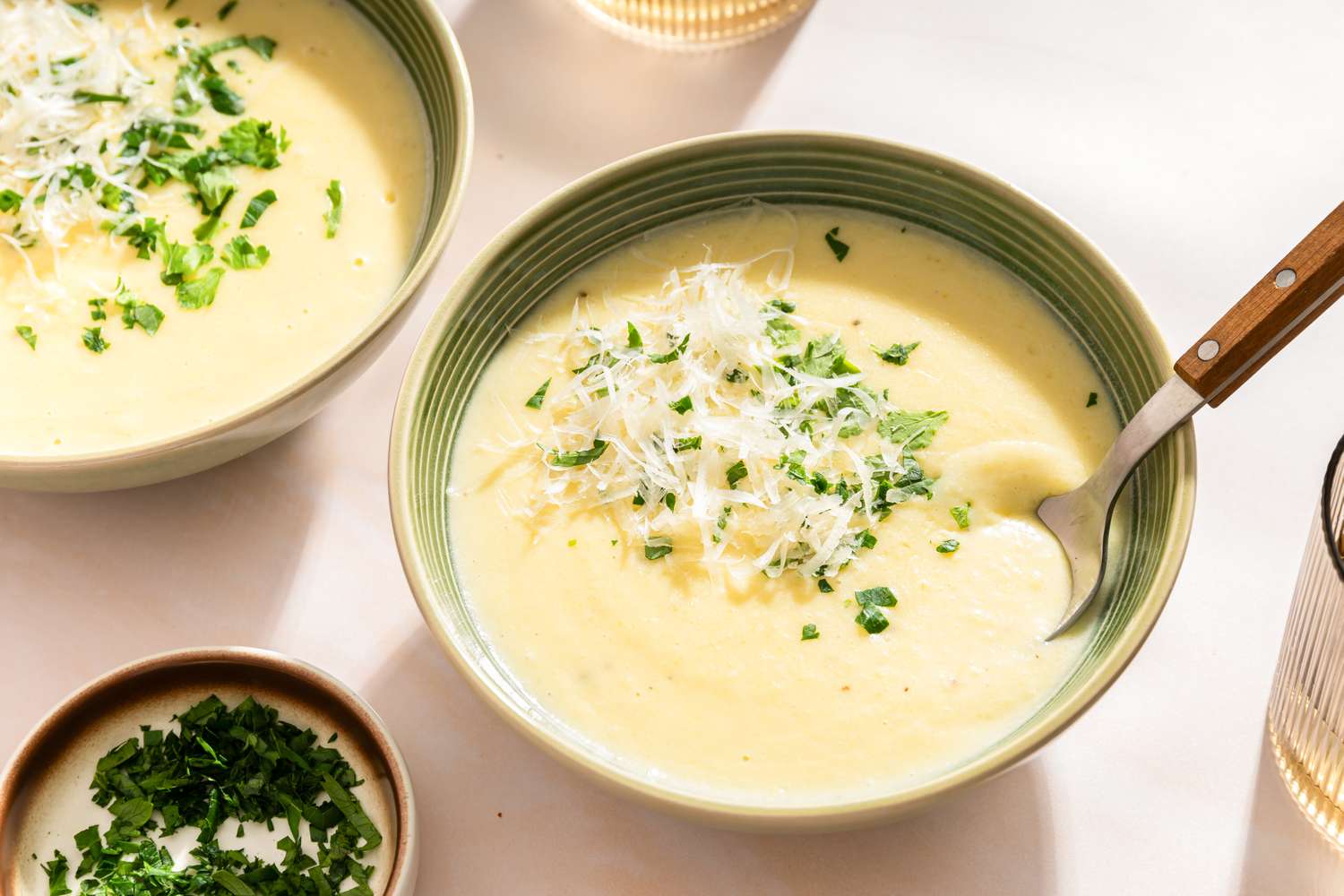 Bowls of potato soup garnished with parsley and grated cheese on a table