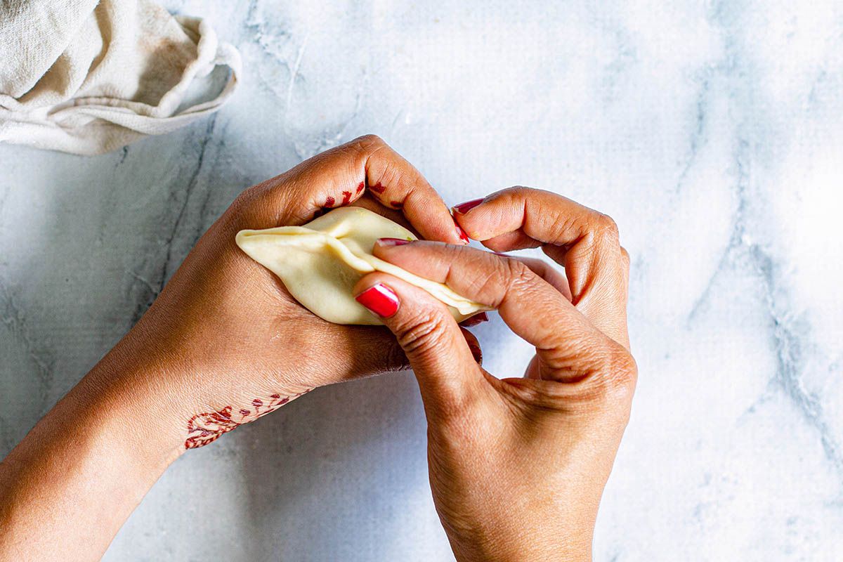 Woman pinching together a cone of dough filled with vegetables in her hands ot make Indian Samosas.
