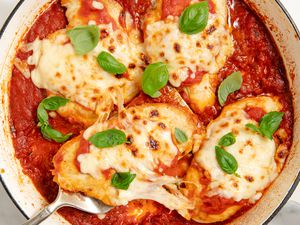 A skillet with four cheese covered chicken breasts in tomato sauce, garnished with basil