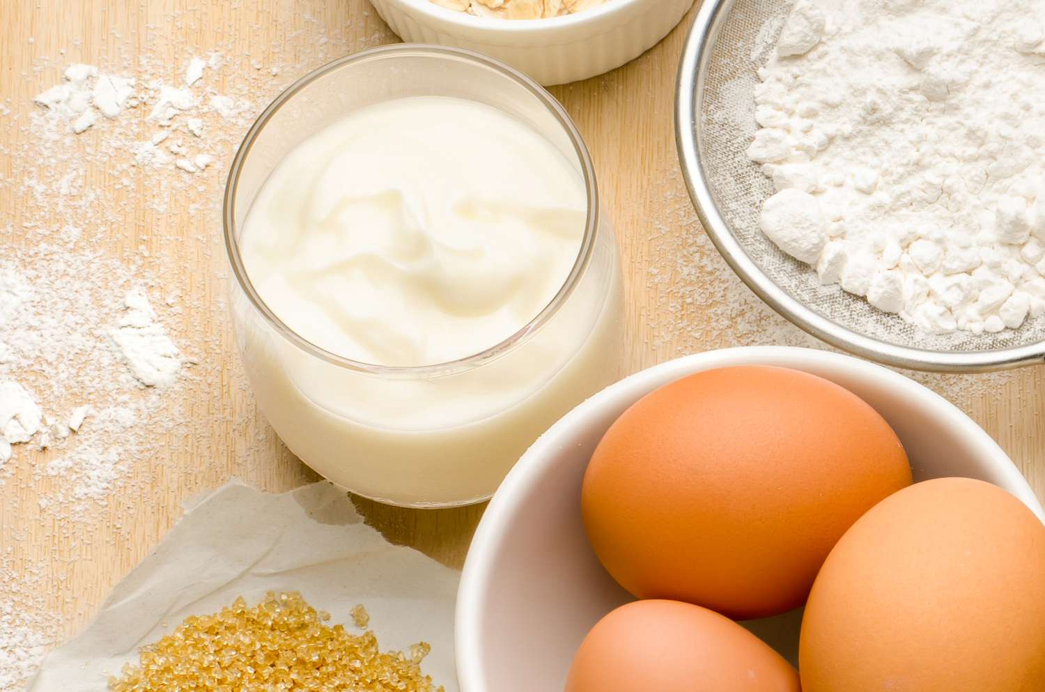 Bowl of eggs yogurt sugar flour and oatmeal on a wooden surface