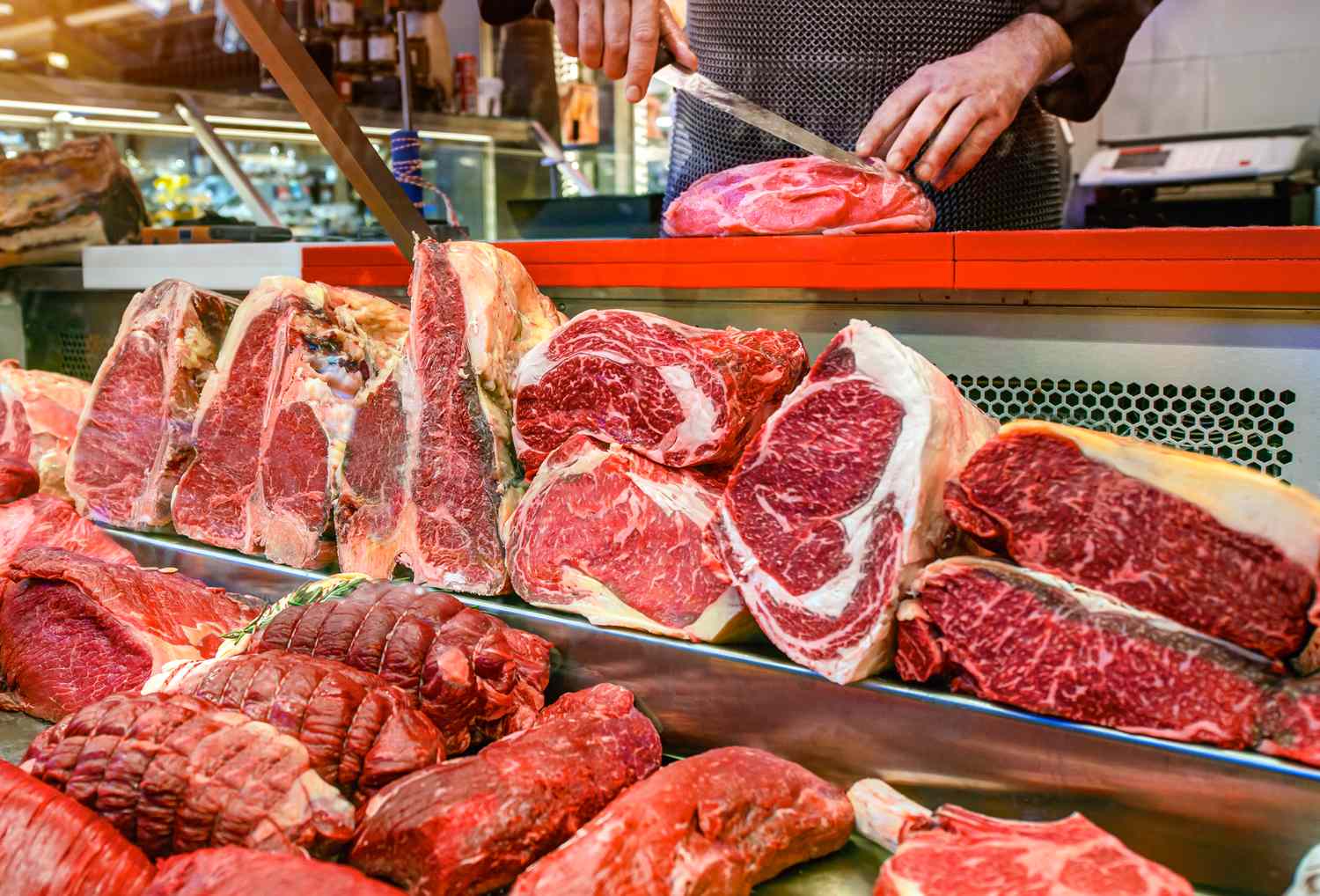 Various cuts of meat displayed on a butchers counter with a person slicing meat in the background