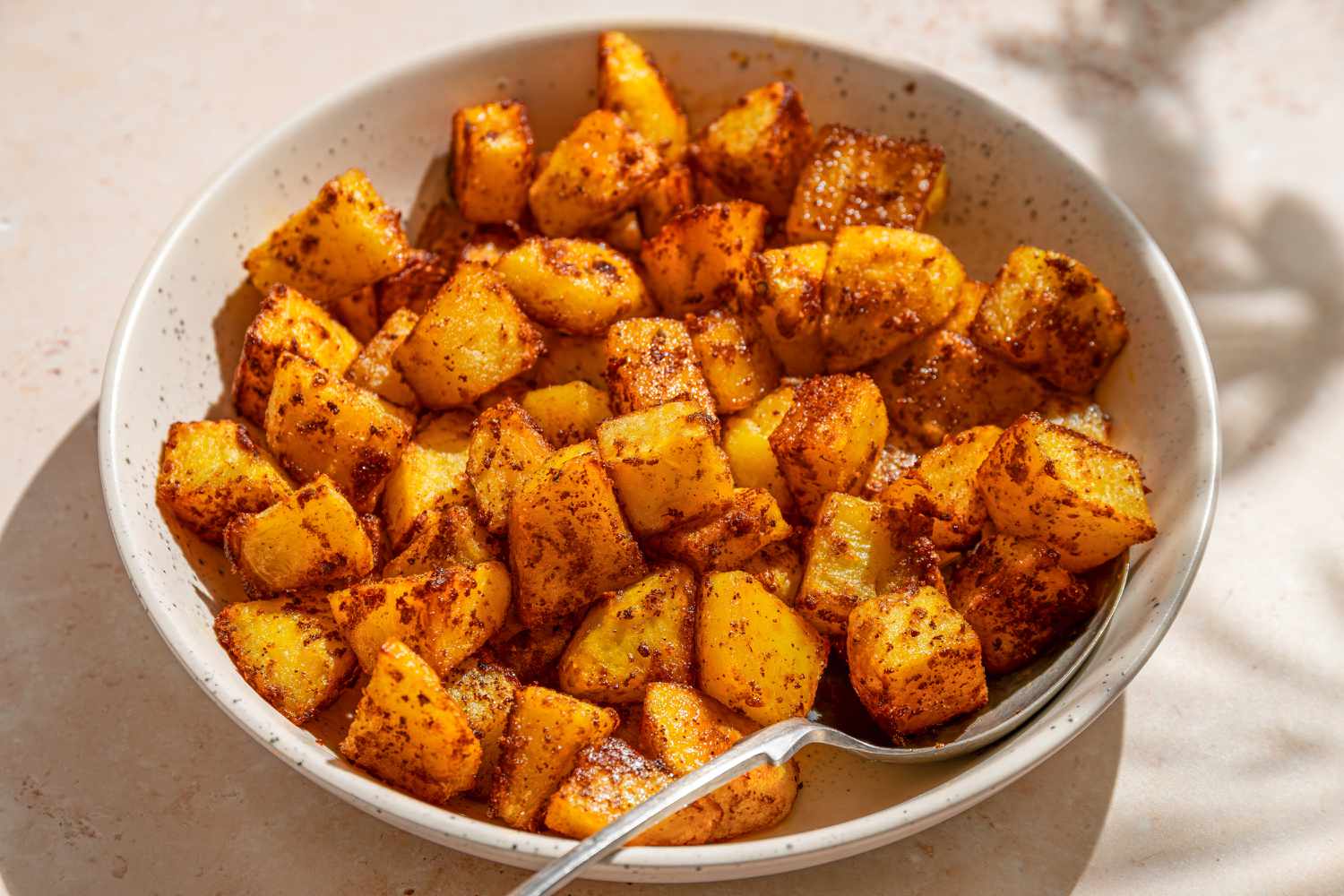 A bowl of roasted potato pieces seasoned with spices, served with a spoon