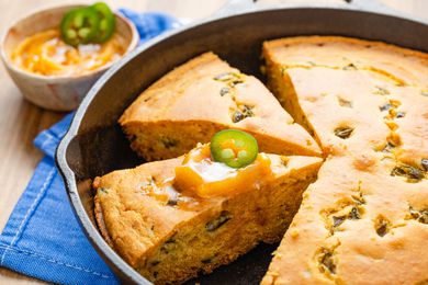 Hot honey cornbread (JalapeÃ±o Honey Cornbread) sliced in a cast iron skillet with one slice topped with hot honey butter