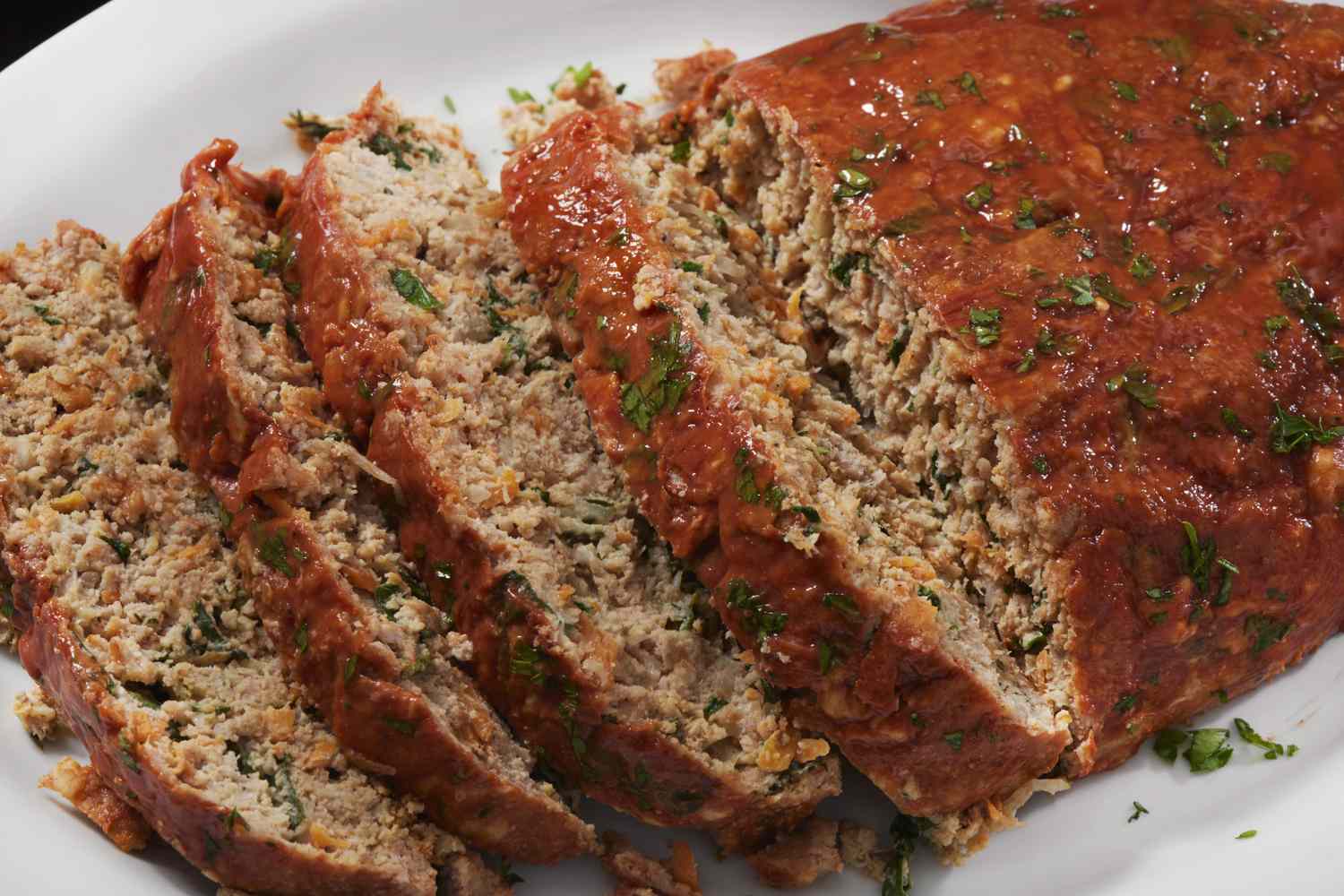 Sliced meatloaf garnished with herbs on a white plate