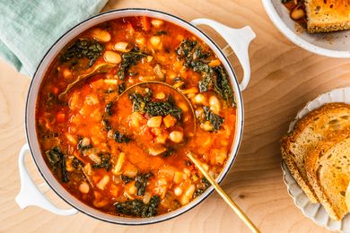 easy Tuscan ribolitta soup in a dutch oven at a table setting with a plate of bread and a kitchen towel