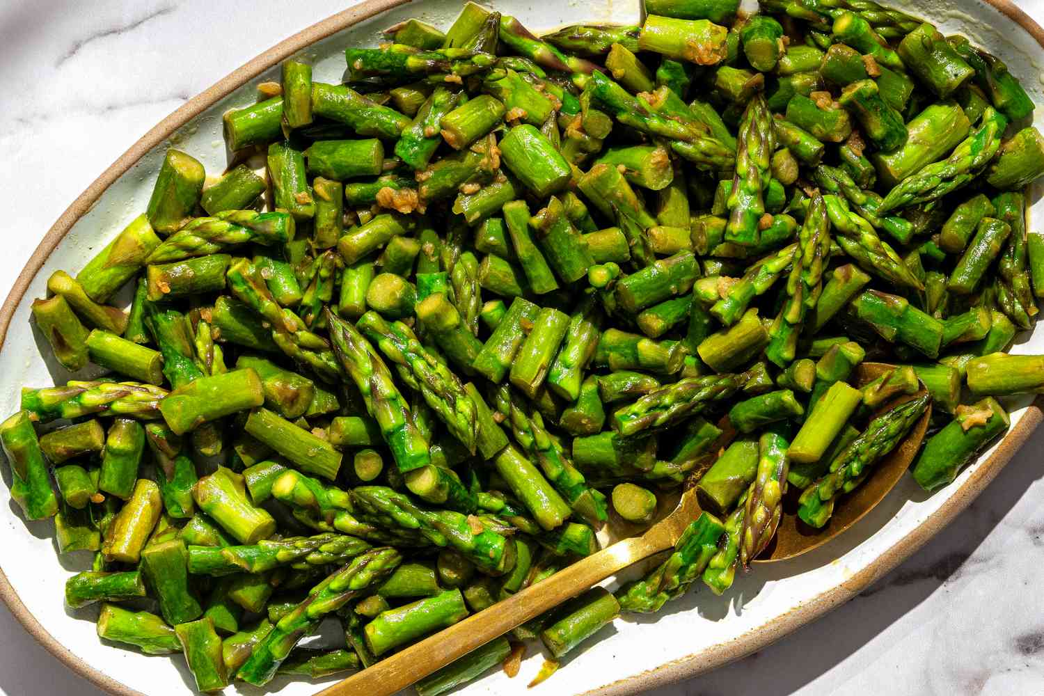 Sauteed asparagus pieces arranged on a platter with a serving spoon.