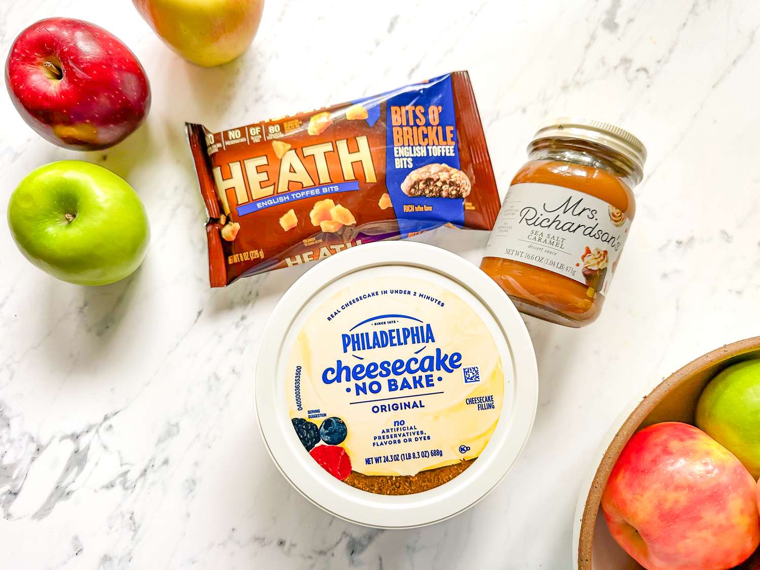 Ingredients for caramel apple dip arranged including apples nobake cheesecake filling a caramel topping and a candy topping