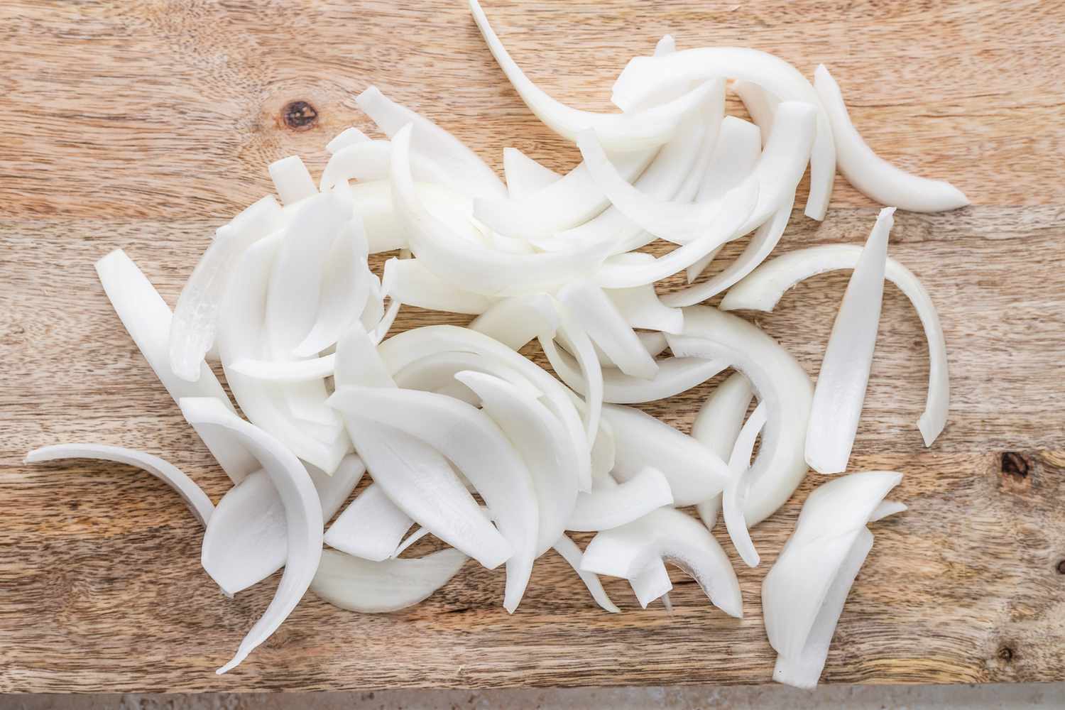 Sliced white onions spread out and resting on a cutting board