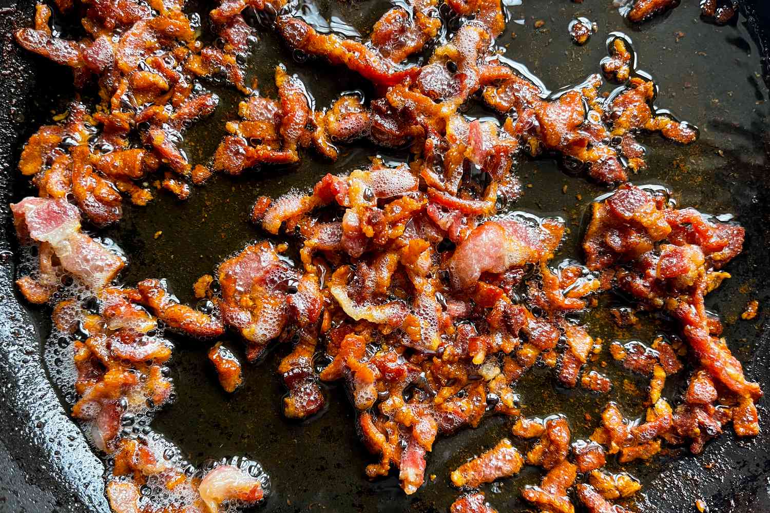 Overhead view of bacon crumbles frying in a skillet