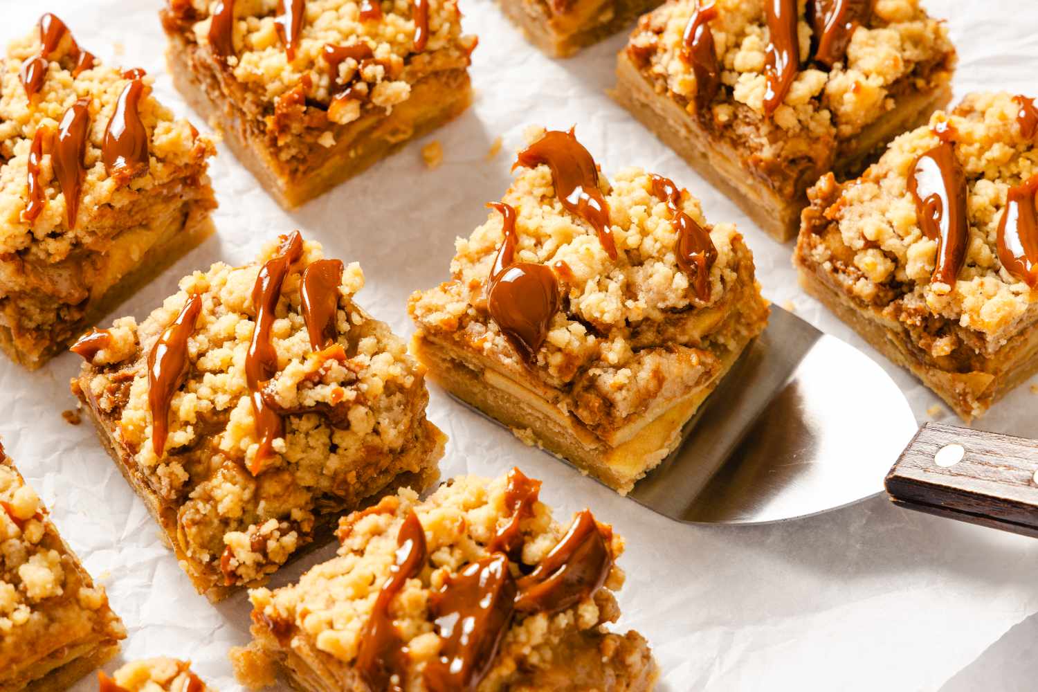 Caramel apple bars with a crumbly topping arranged on parchment paper
