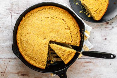 Southern Cornbread in a Skillet with a Piece Cut Out and Another Piece on a Plate