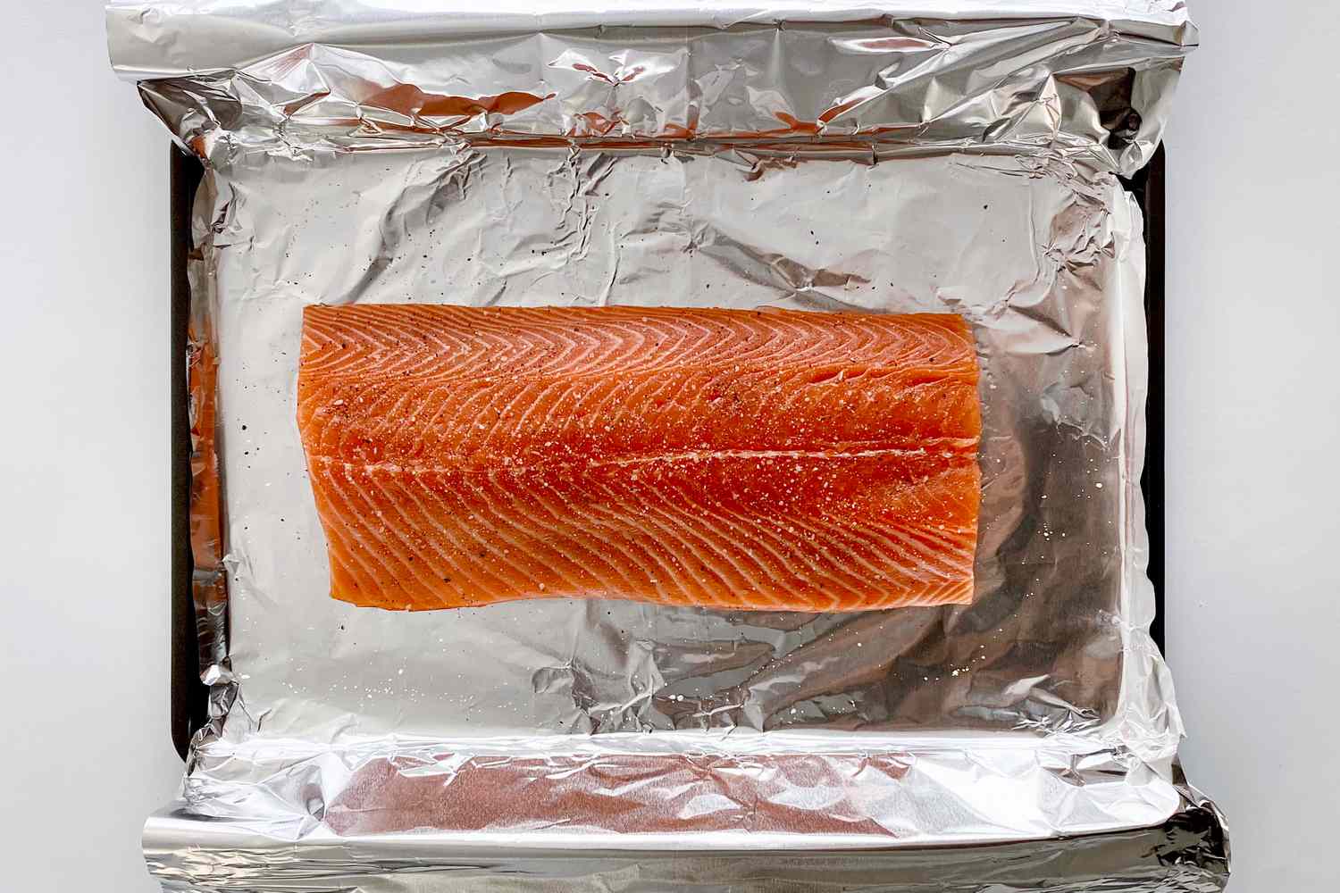 Unbaked salmon on a foil lined baking sheet sprinkled with salt and pepper