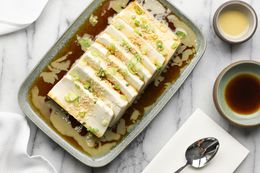 Platter of Silken Tofu with Sesame Soy Sauce Next to a Small Bowl with More Soy Sauce, Another Small Bowl with Sesame Sauce, a Spoon on a Napkin, and a Kitchen Towel