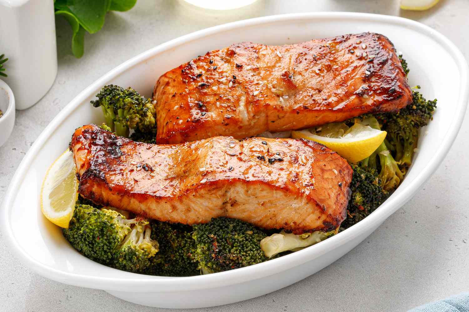 Two baked salmon fillets on top of broccoli in a white baking dish