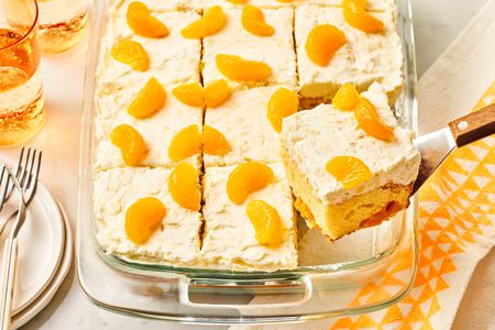 Angled view of a baking dish of pineapple and mandarin orange cake with a slice being removed with a spatula