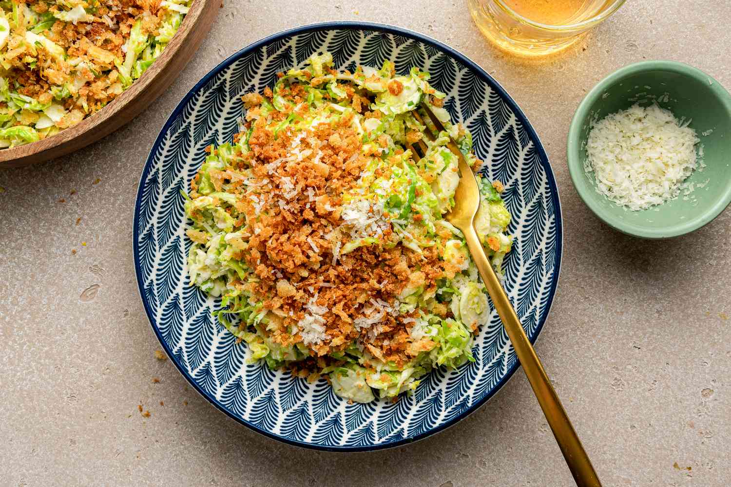 Serving of Brussels Sprouts Caesar Salad with Lemony Breadcrumbs in a Bowl with a Fork Next to a Larger Bowl with More, a Bowl with Shredded Parmesan, and a Glass