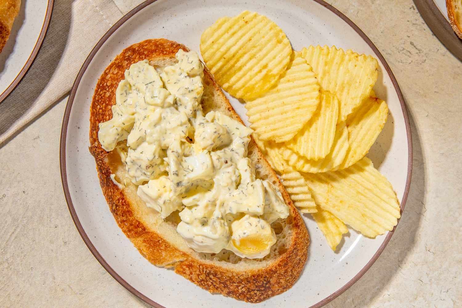 Egg salad served on bread with a side of potato chips on a plate