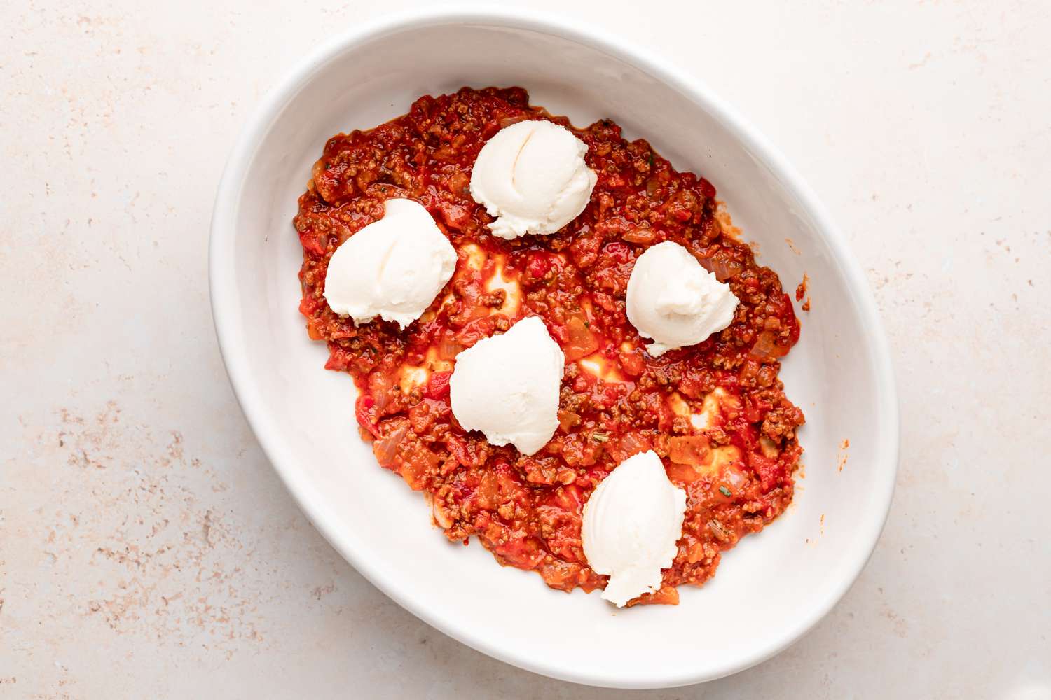 Oval dish with sauce and cheese inside to make ziti pasta.