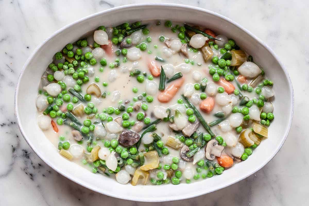 Vegetarian Shepherd’s Pie Recipe -- white casserole dish filled with carrots, peas, onions, mushrooms and cream sauce