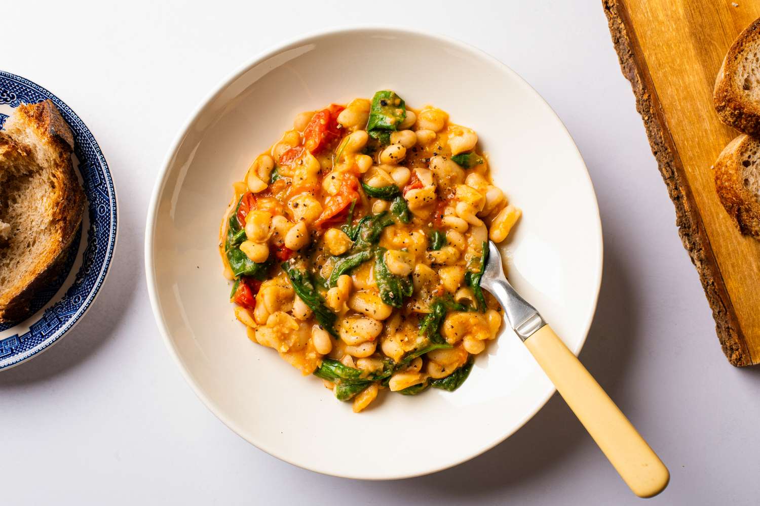 A plate of stewed beans with tomatoes and spinach served alongside bread