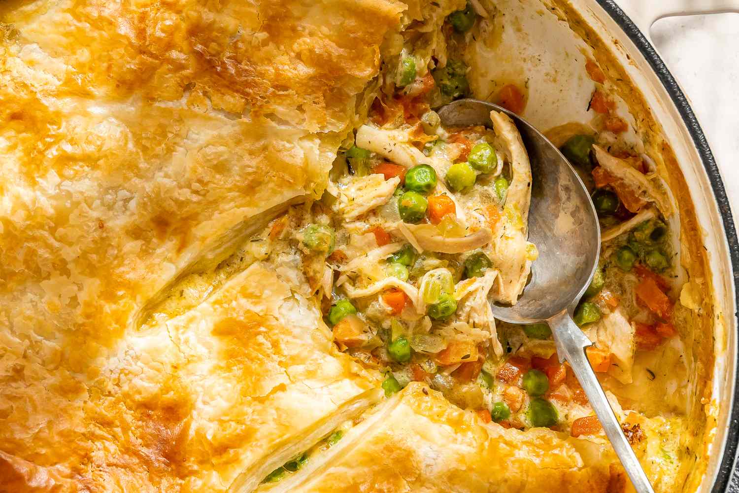 A pot pie in a baking dish partially served with a metal spoon