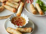 Dipping a spring roll into a sauce with more spring rolls on the plate and on a platter behind it.