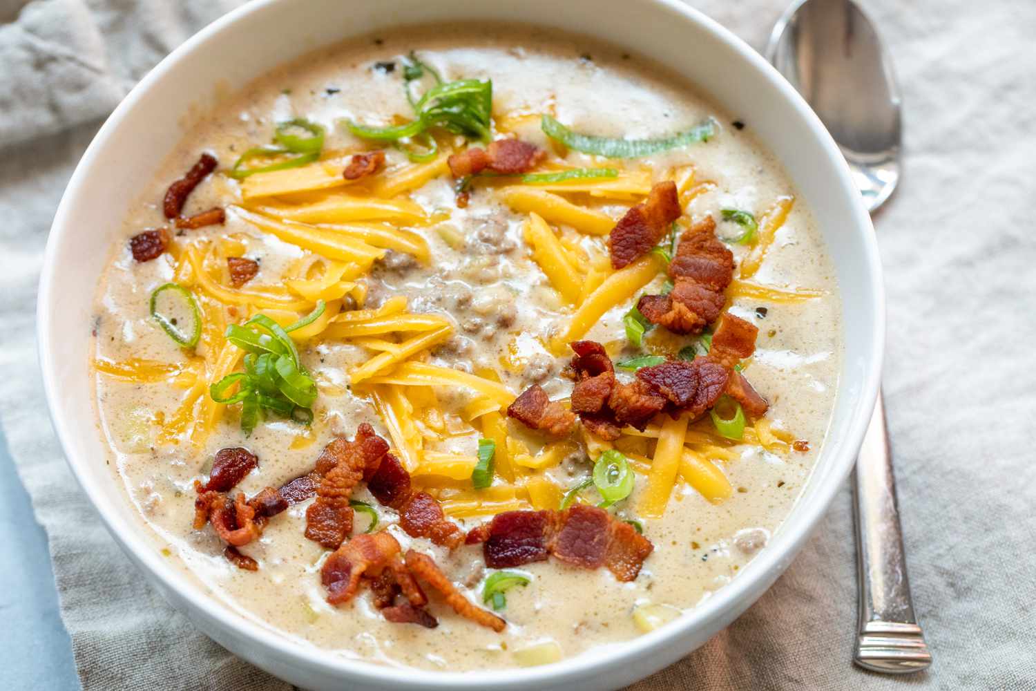 Cheesy bacon cheeseburger soup in white bowl. 