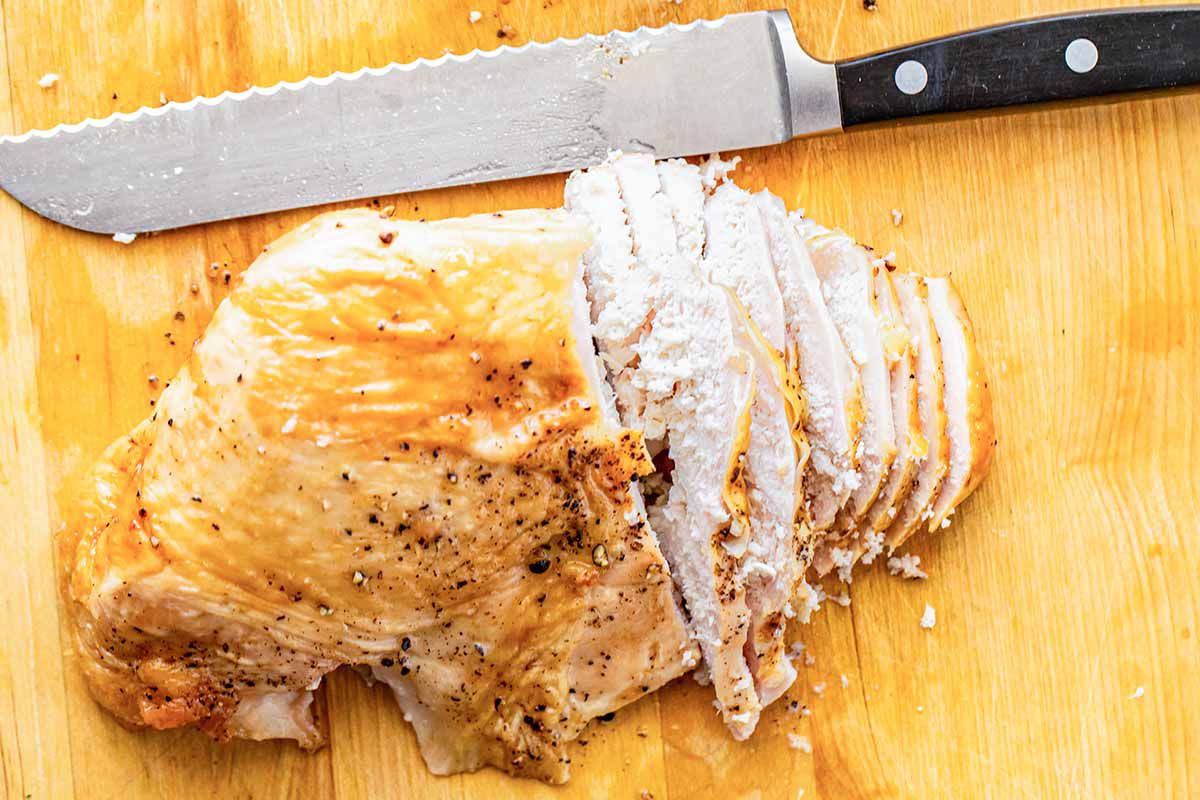 Roast turkey sliced on a cutting board and a knife for a turkey club sandwich.
