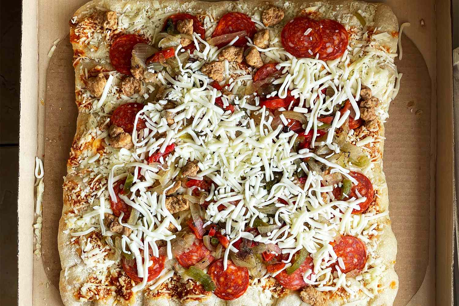 A prepared take-and-bake pizza with pepperoni, cheese, and various toppings in a cardboard baking tray
