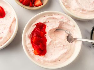 A bowl of strawberry mousse garnished with strawberry topping with additional bowls nearby