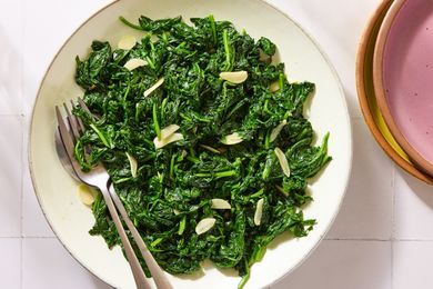 A bowl of sauted spinach garnished with garlic slices two forks resting on the side