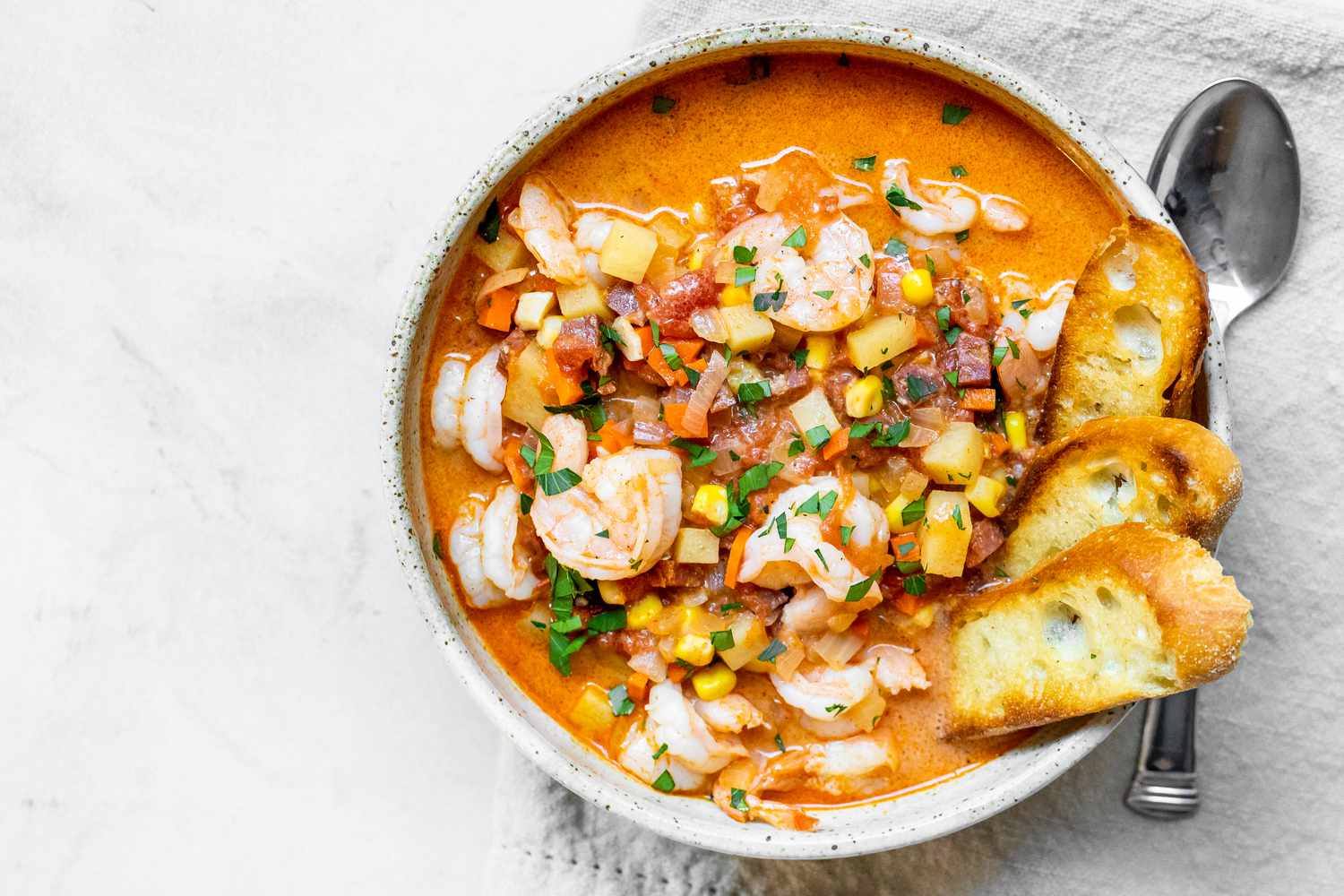 Bowl of Shrimp and Chorizo Chowder Topped with Parsley and Slices of Toasted Baguette