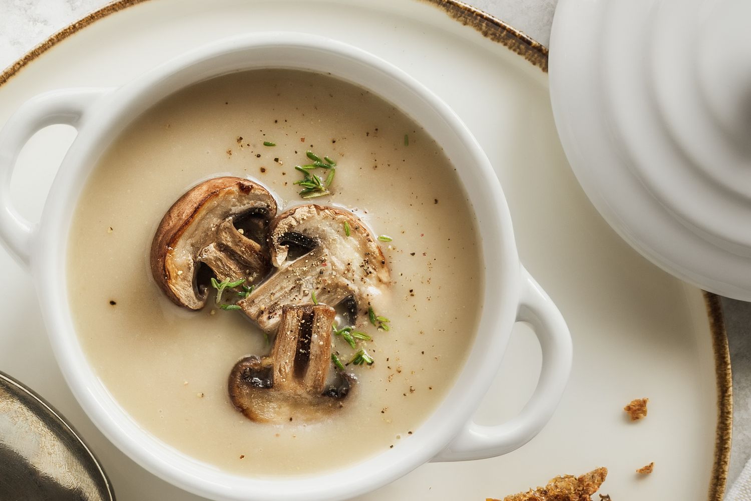 A bowl of mushroom soup garnished with sliced cooked mushrooms and herbs