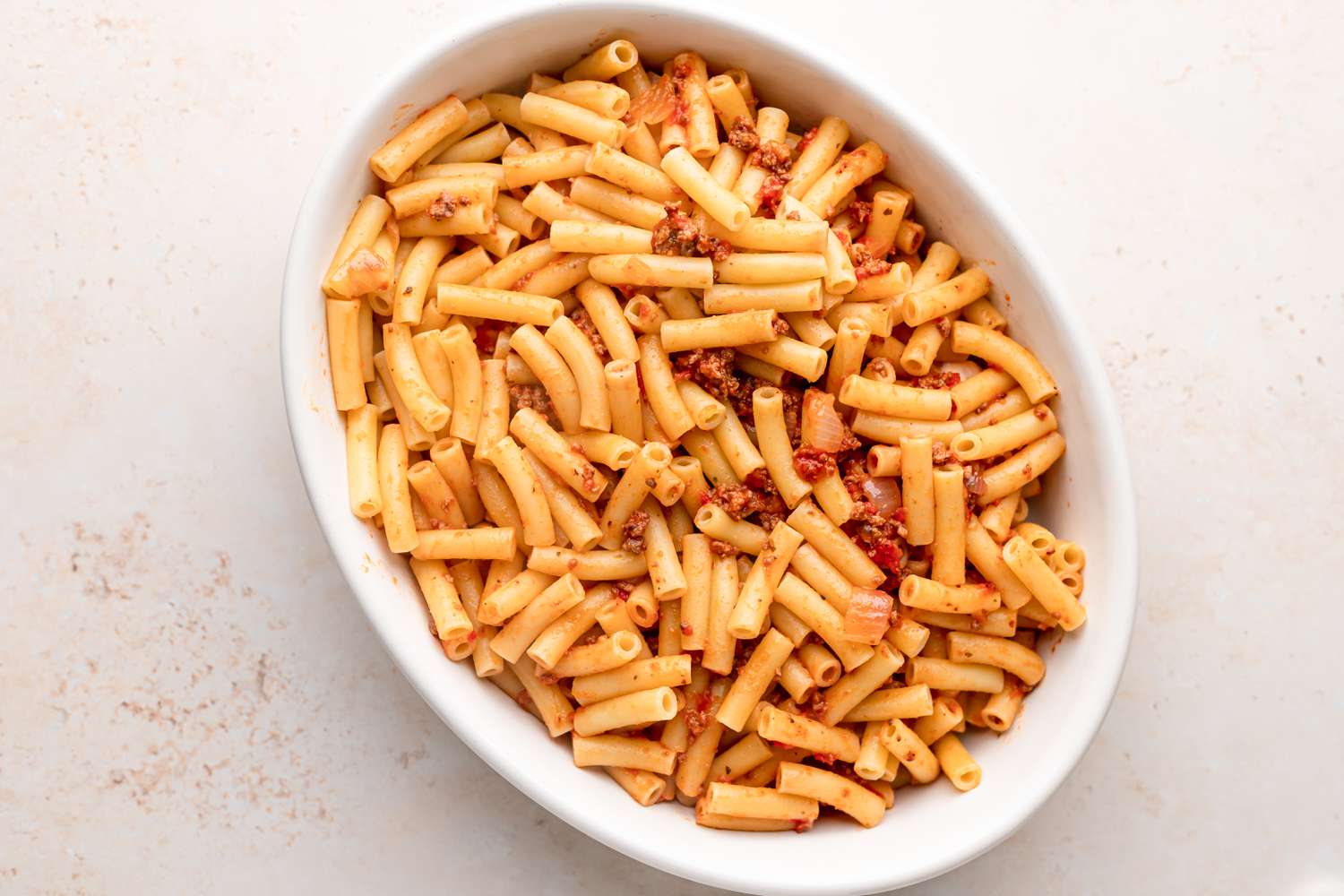 Ziti pasta with sauce in an oval baking dish.