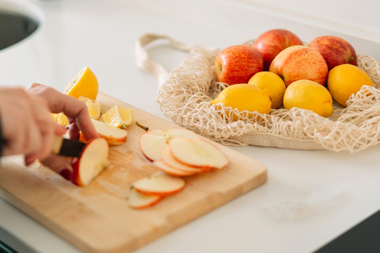 Chopped apple slices on a cutting board with whole apples and lemons in a bag on the table