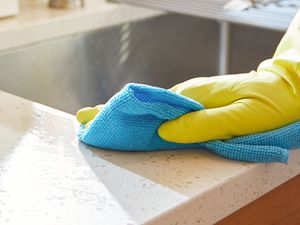 A house cleaner cleaning and sanitizing kitchen worktop and surfaces wearing rubber gloves and using a blue towel