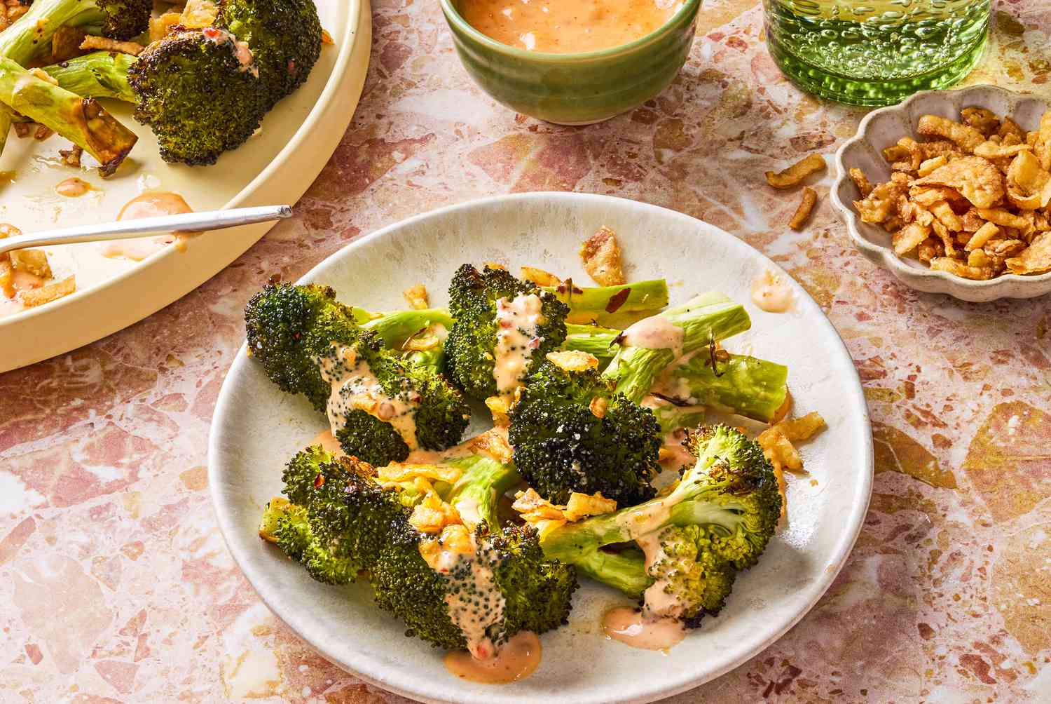 plate of Bang Bang Broccoli smothered with Bang Bang sauce and garnished with fried onions, small dish of fried onions and another small dish of sauce on the side