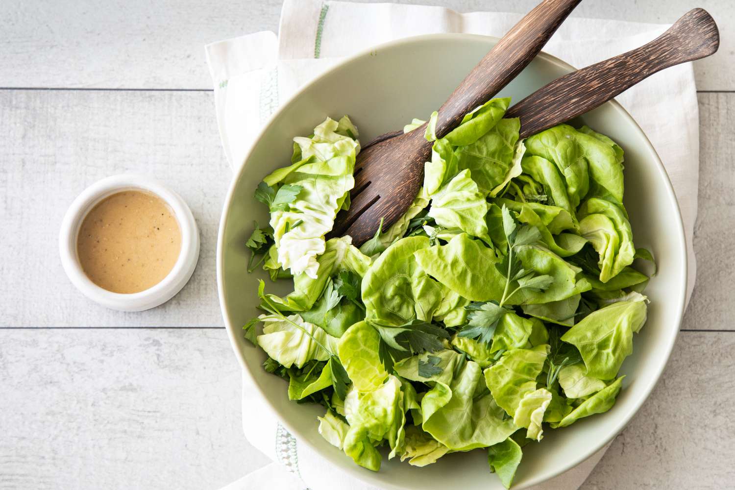 Large Bowl of Green Salad with Fresh Herbs with Serving Utensils and a Small Bowl of Red Wine Vinaigrette 