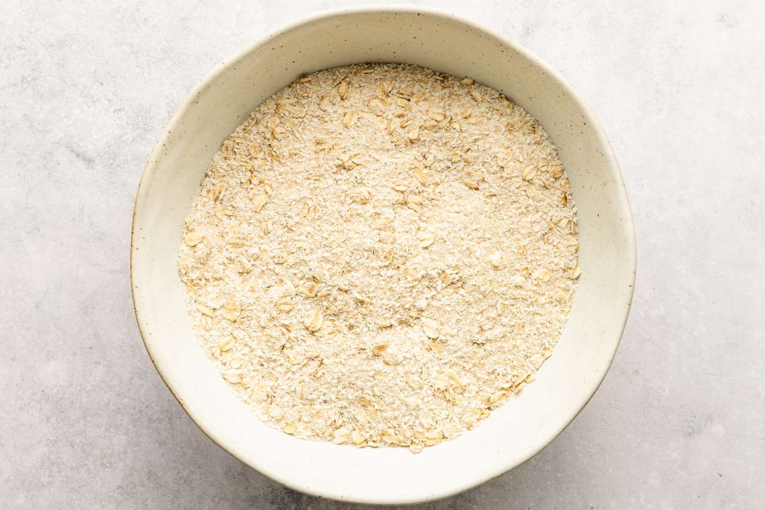 Oats and flour for the Anzac Biscuits recipe in a white bowl