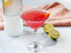 Cosmopolitan ingredients on a counter with a cosmo drink in front.
