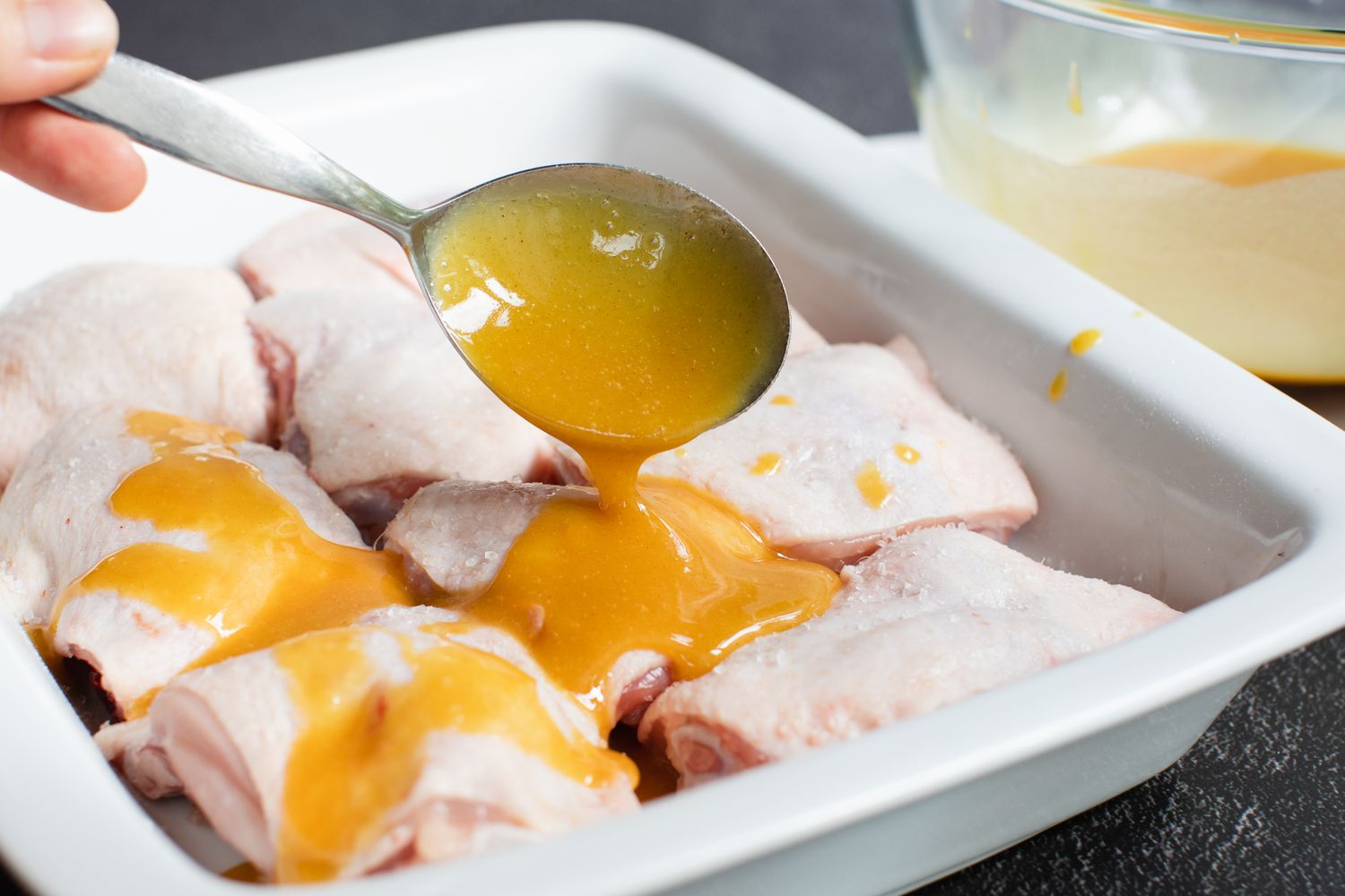 Spooning honey mustard sauce over chicken thighs in a casserole dish.
