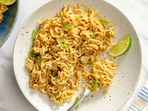 Plate of peanut chicken noodles garnished with a lime wedge