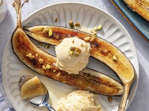 Caramelized bananas served with scoops of ice cream topped with chopped nuts on a white plate