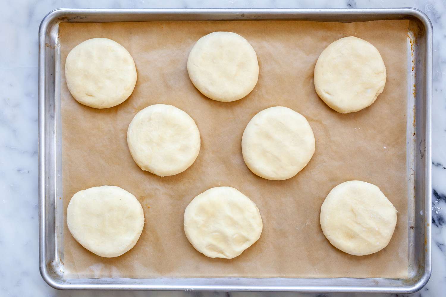 Dough rounds slightly flattened on a baking sheet for homemade hamburger buns.