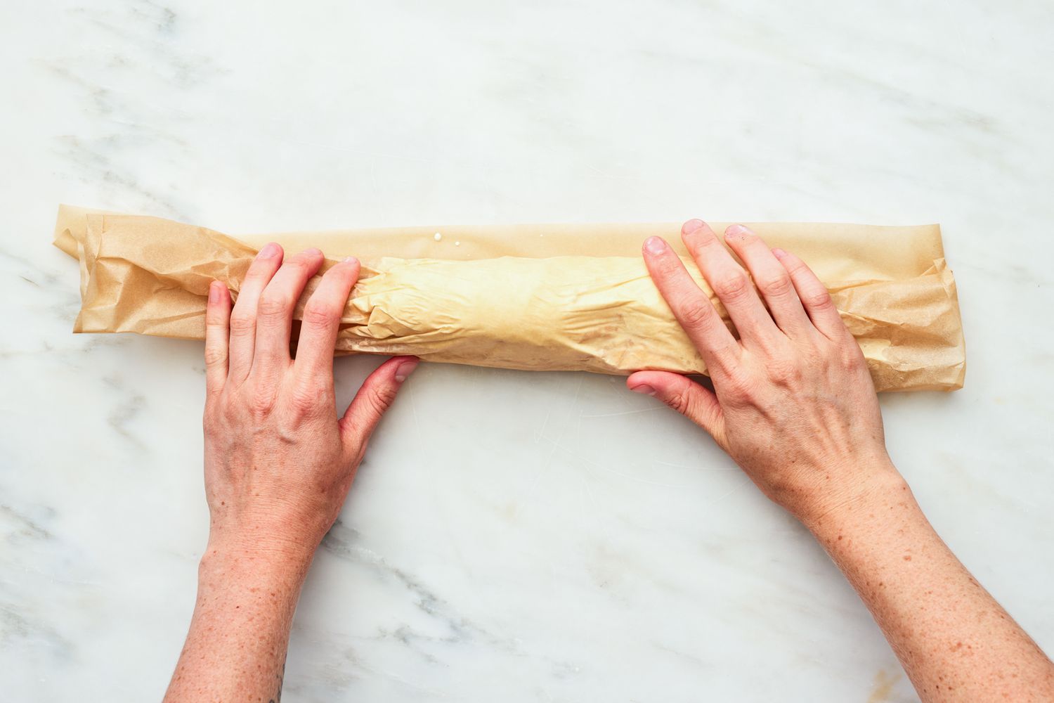 Two Hands Rolling the Ice Cream in the Parchment Paper Into a Log for 2-Ingredient Ice Cream Sandwich Recipe