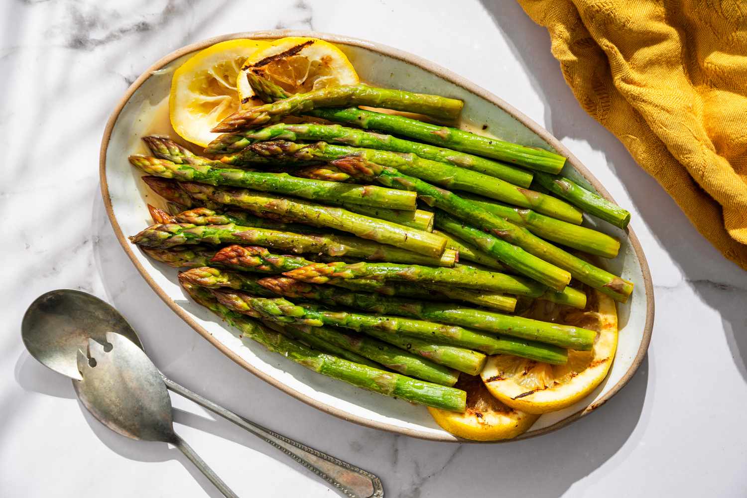 Plate of grilled asparagus with lemon slices, served with utensils on the side