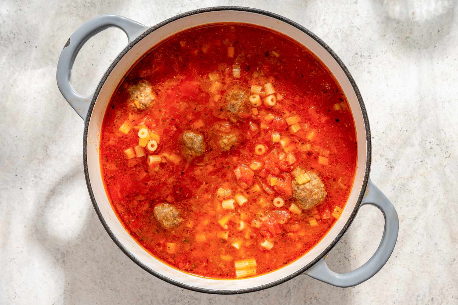 Overhead view of a pot Italian Meatball Soup recipe after adding diced tomatoes, chicken broth, and Italian seasoning and meatballs