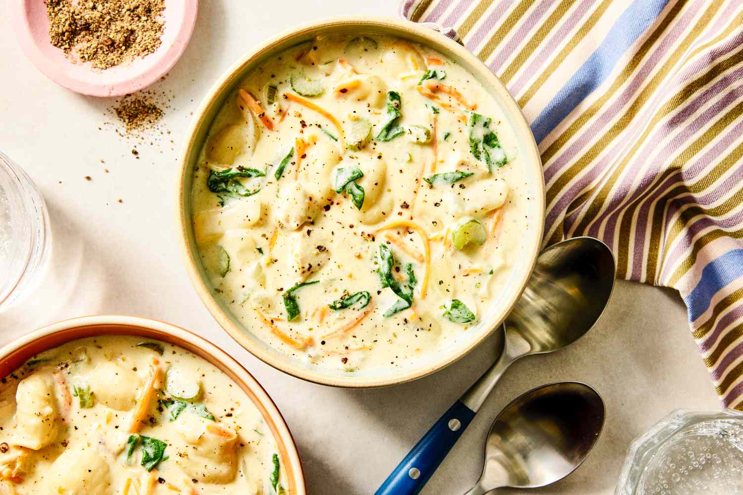 Bowls of creamy gnocchi soup garnished with pepper and surrounded by tableware